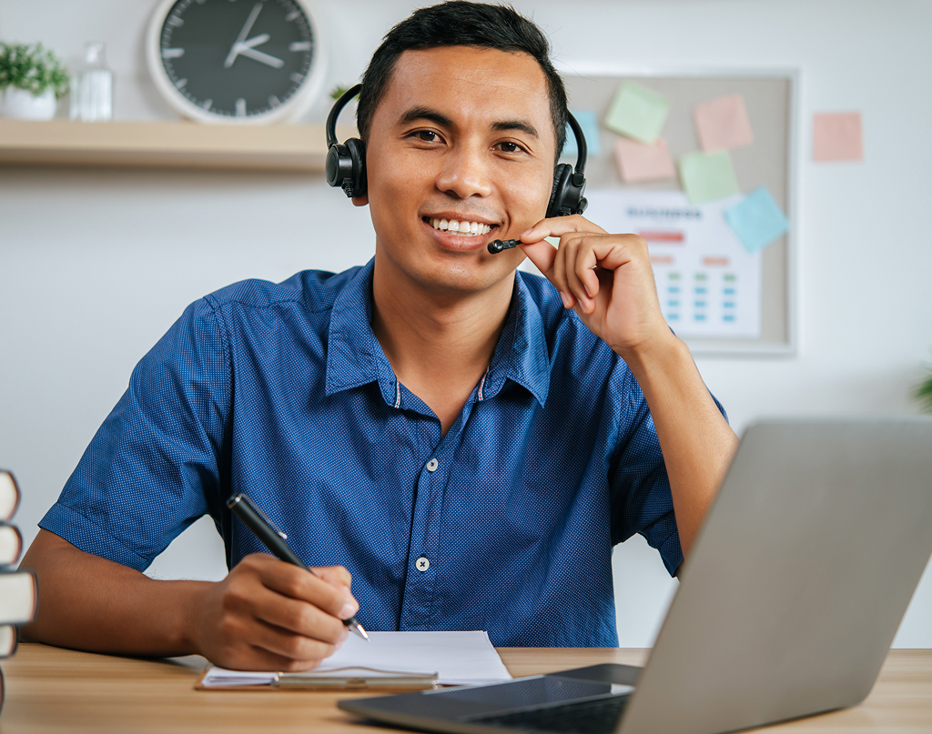 Man with headphones working on a laptop surrounded by papers at his office desk